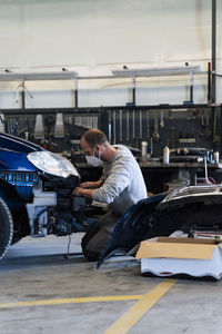Auto mechanic kneeling and repairing car in garage