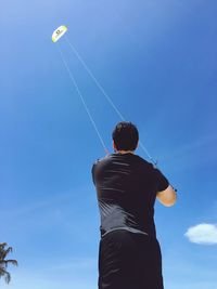 Low angle view of man holding umbrella against blue sky