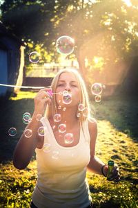 Portrait of woman blowing bubbles while standing on field during sunny day