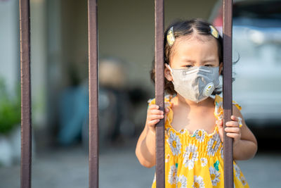 Girl standing at fence wearing medical face mask to prevent flu, pollution and covid 19.