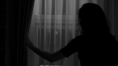 Rear view of silhouette woman standing by window at home