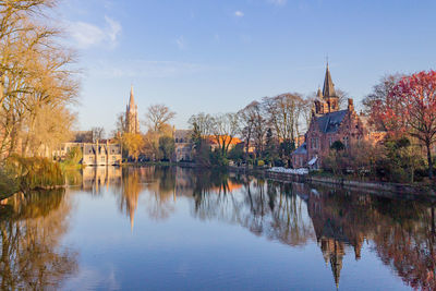 Reflection of building and trees on river against sky