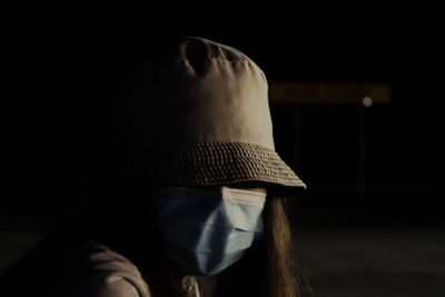 Close-up of young woman wearing mask sitting in darkroom