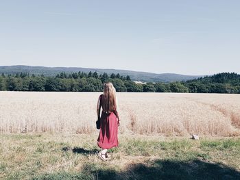 Rear view of woman walking on grass in farm against sky