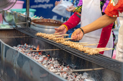 Woman grilled meat ball on charcoal in street food market.