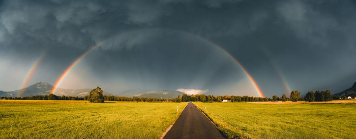 Panoramic image of glowing double rainbow above fields and road in salzburg, austria