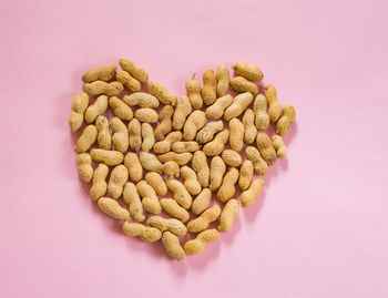 High angle view of heart shape made with peanuts against pink background