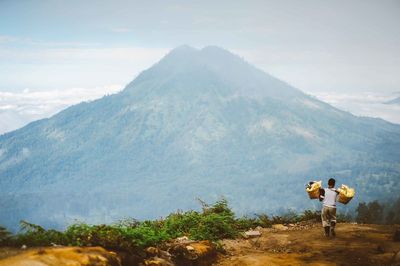 Rear view of man carrying baskets while walking on mountain 