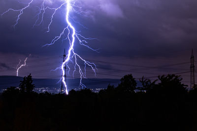 Lightning over silhouette trees against dramatic sky at night