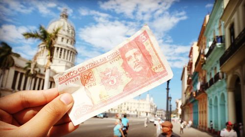 Cropped hand holding paper currency on road in city