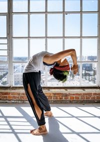 Side view of woman exercising against window