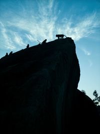 Low angle view of silhouette bird perching on mountain against sky