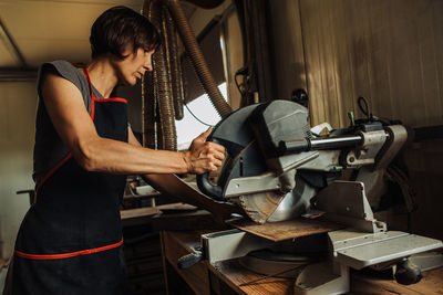 Middle aged woman cutting wood in a sliding mitre saw