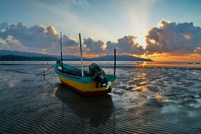 Motorboat moored at beach against sky during sunset