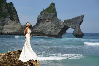 Portrait of woman standing on rock by sea against clear sky