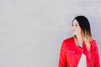 Young woman looking away while standing against wall