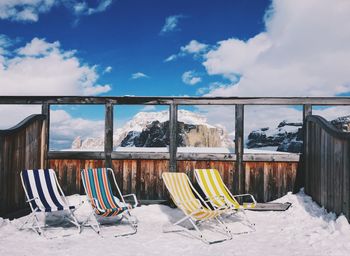 Chairs on snow covered land against sky