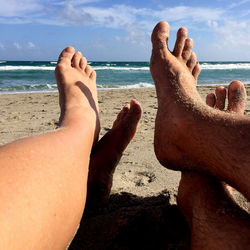Low section of friends with crossed legs on sand at beach