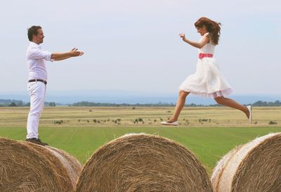 Woman jumping on hay bales towards embracing man