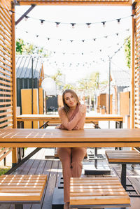 Happy charming young woman is sitting at a table in an outdoor cafe and waiting