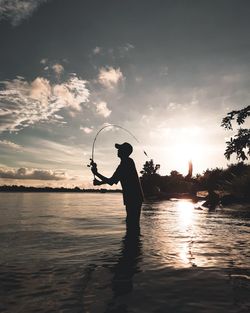 Silhouette man fishing in lake against sky during sunset