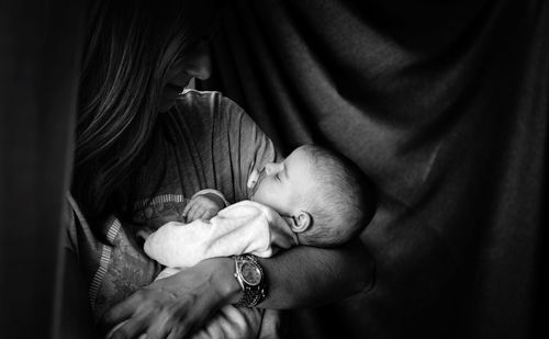 Mother carrying son while standing by curtain at home