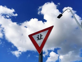 Low angle view of road sign and street light against sky