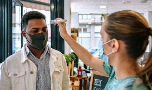 Woman checking temperature of customers wearing mask in restaurant