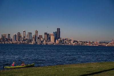 Cityscape by sea against clear blue sky