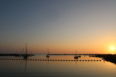Sailboats in sea against clear sky during sunset