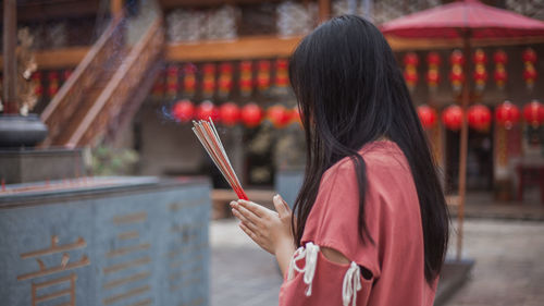 Rear view of woman holding umbrella against building