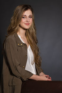 Portrait of young woman with blond hair sitting on stool against black background