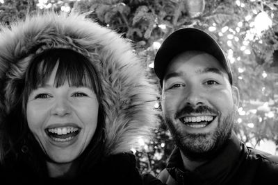 Portrait of smiling friends standing against tree during winter