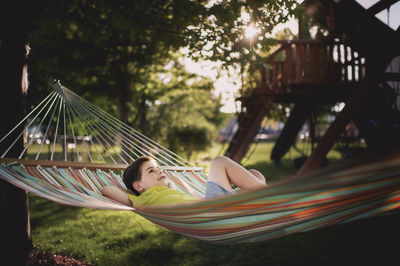 Boy with hands behind head lying in hammock at park