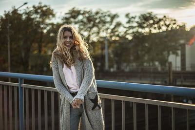 Portrait of smiling young woman standing by railing