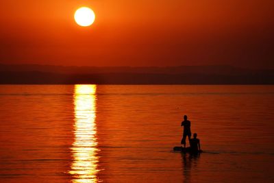 Silhouette people on sea against sky during sunset