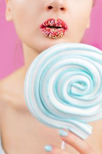 Close-up of woman holding blue lollipop against pink background