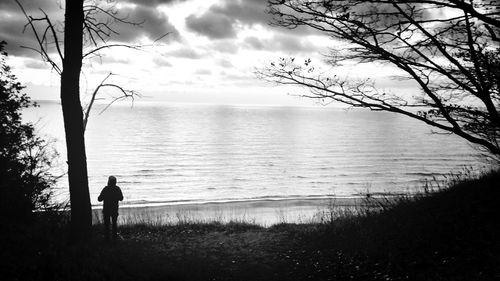 Silhouette of man walking on shore against sky