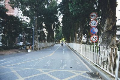 Road sign by trees on street in city