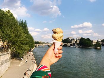 Cropped hand of woman holding ice cream against sky in city