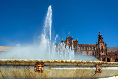 Fountain in front of building against blue sky