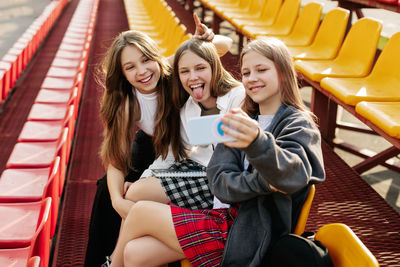 Three charming friends take selfies on their phone at the school stadium. the concept of friendship