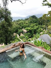 Young woman enjoying in swimming pool against trees in forest