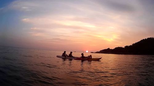 People kayaking at sea against sky during sunset