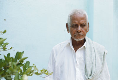 Portrait of man standing by plant against wall