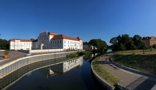 Buildings by river against clear blue sky