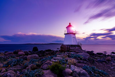 Lighthouse by sea against sky during sunset