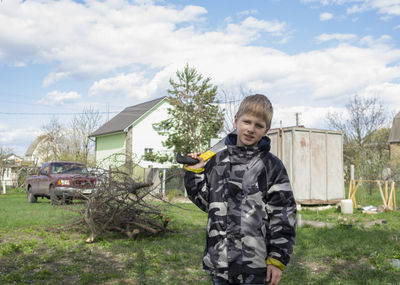 Portrait of boy with work tool standing in yard