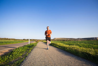 Full length of man running on road against clear sky