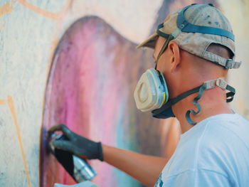 Side view of young man spraying graffiti on wall